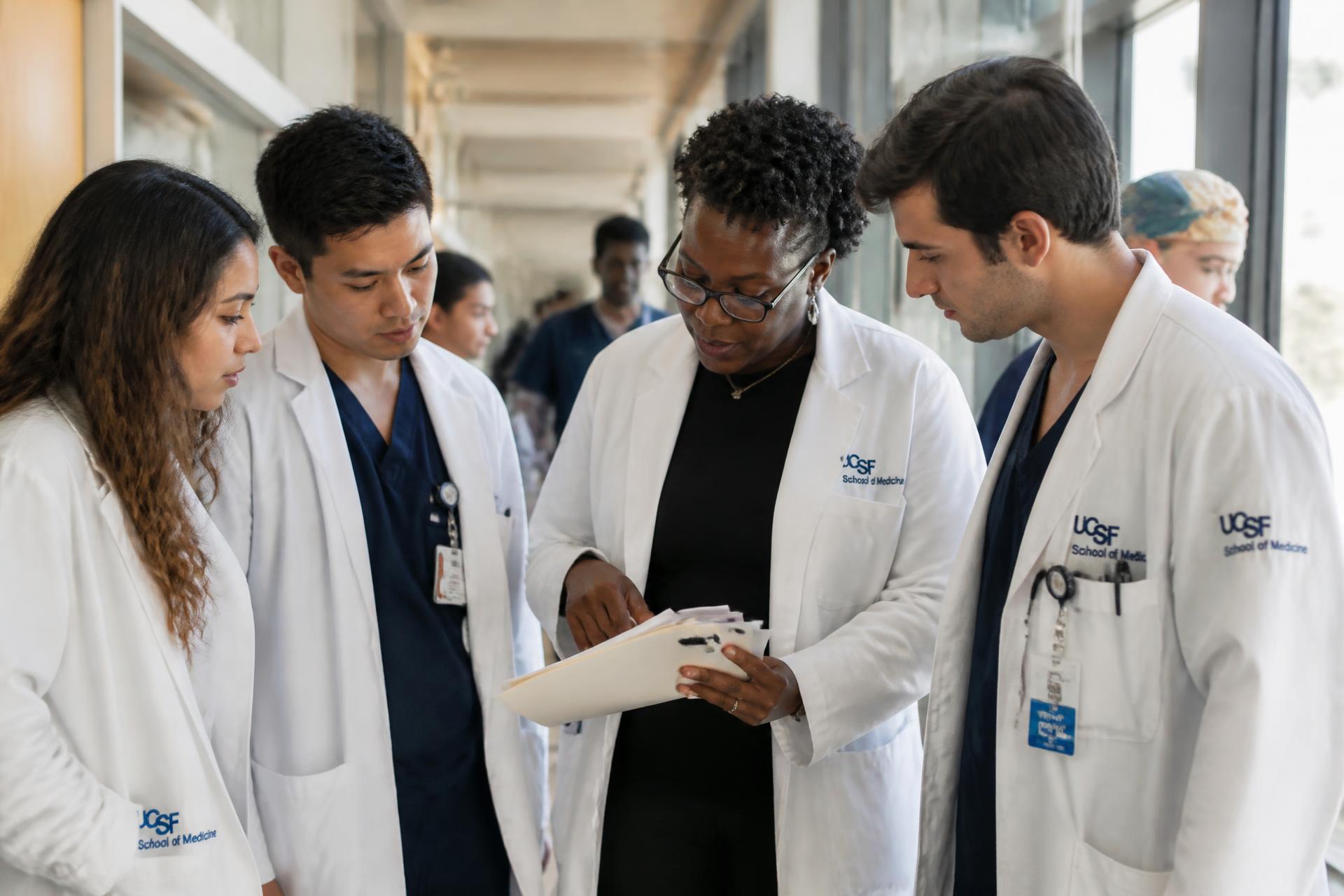 Attending physician reviewing patient notes with medical students in a teaching hospital corridor